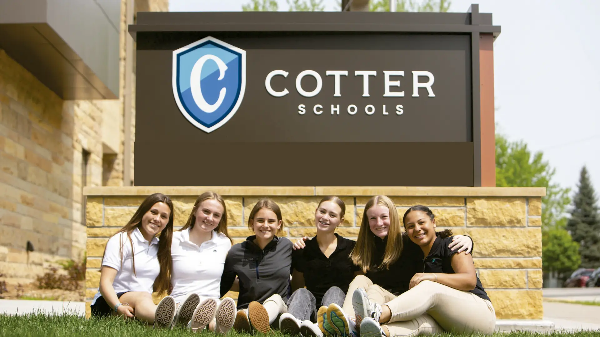 alumnas sentadas en el césped debajo del cartel de la escuela en el curso escolar en estados unidos en Cotter Schools