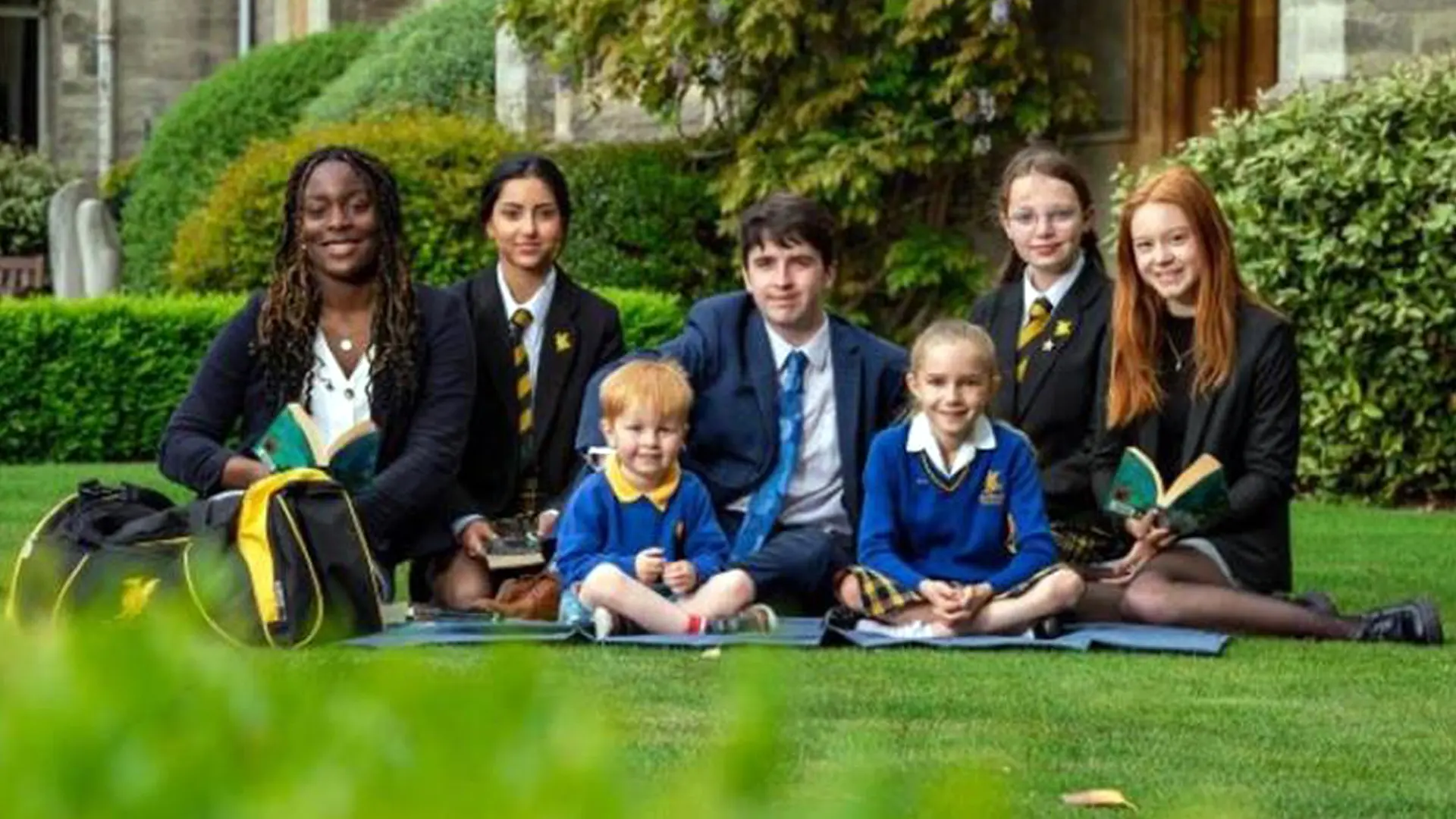 alumnos de todos los cursos juntos en el cesped del campus en el curso escolar en inglaterra en Queen’s College