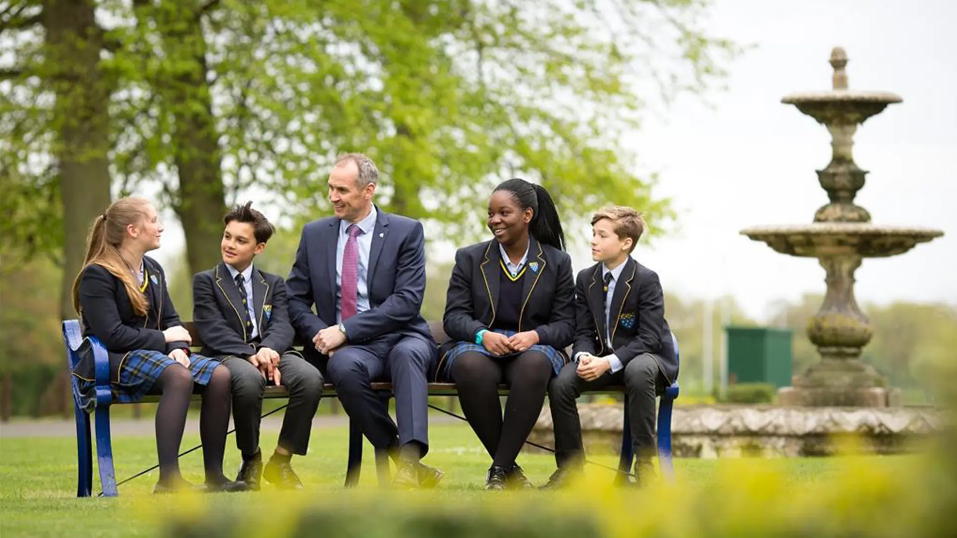 alumnos y profesor hablando sentados en un banco del campus en el curso escolar en inglaterra en Ratcliffe College